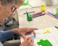 Ältere Frau zeichnet mit bunten Stiften Puzzle-Teile in der Tagespflege Homberg