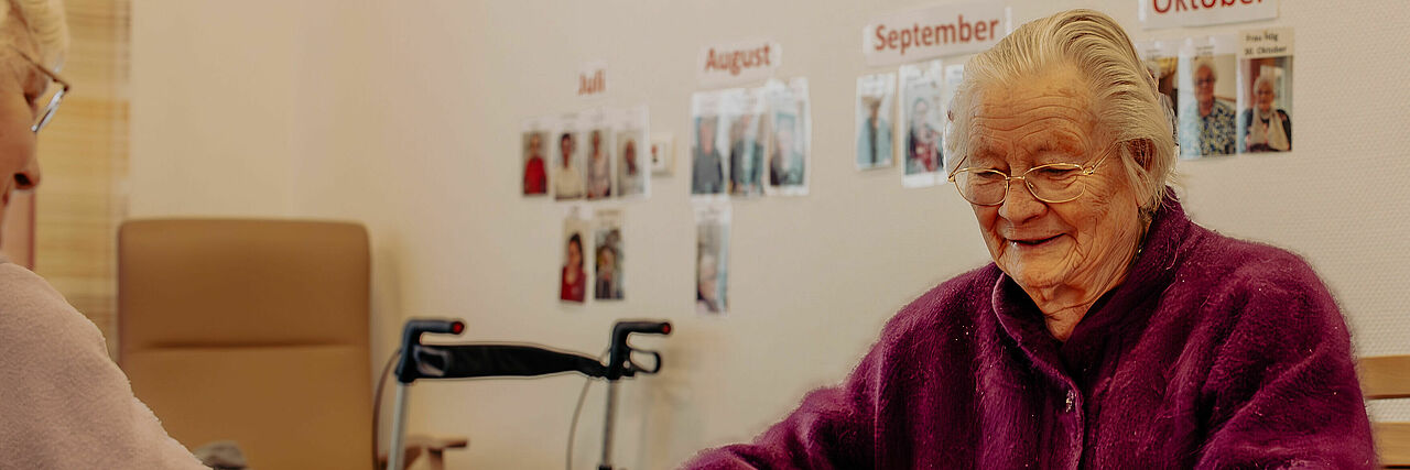 Ältere Frau sitzt in einem Altenheim am Tisch und schaut nach unten