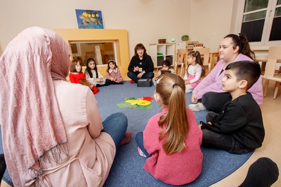 Kinder und Erzieherinn sitzen im Kreis