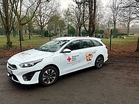 Zu sehen ist ein weißes Auto von der Seite, mit der Aufschrift ,,Kita Flitzer" und dem Logo des DRK Duisburg. Es handelt sich hierbei um den neuen Kita Flitzer